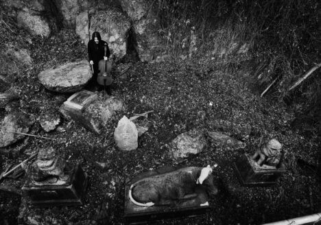 Benjamin Skepper with cello among stone shrine guardians, seen from above